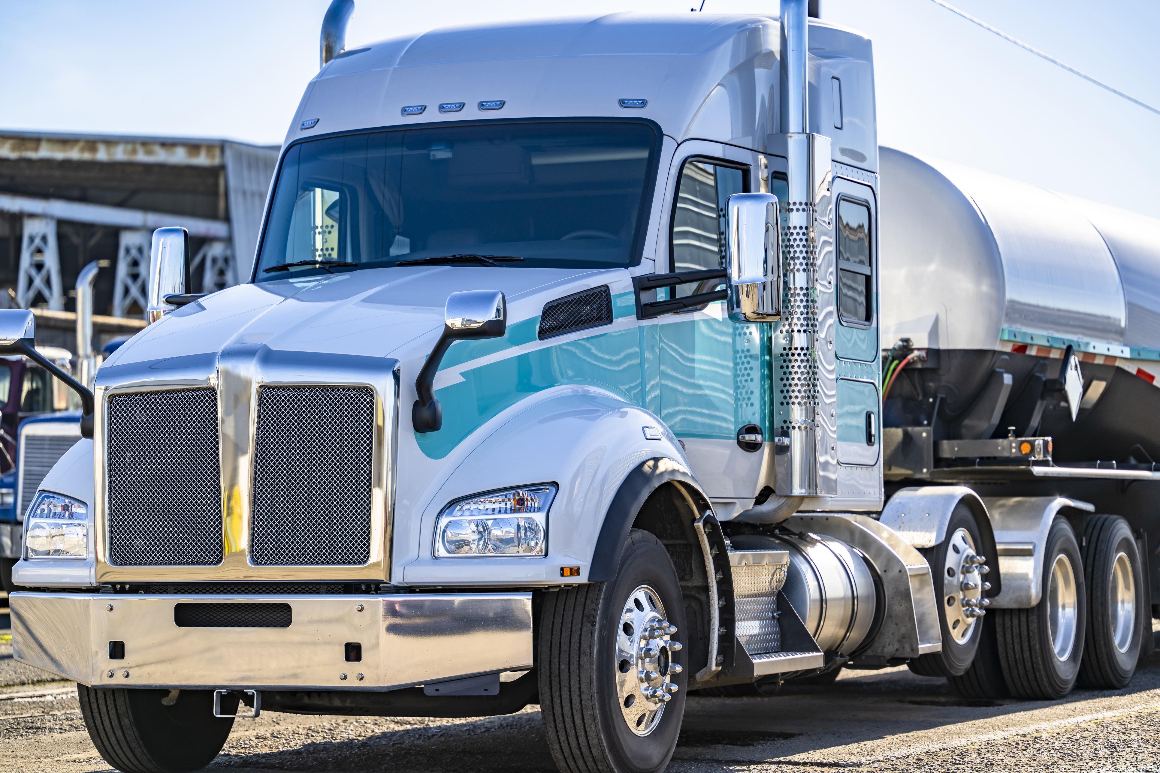 Industrial white and turquoise long haul bonnet big rig semi truck tractor with extended cab for truck driver rest and tank semi trailer standing on the industrial parking lot waiting for next load